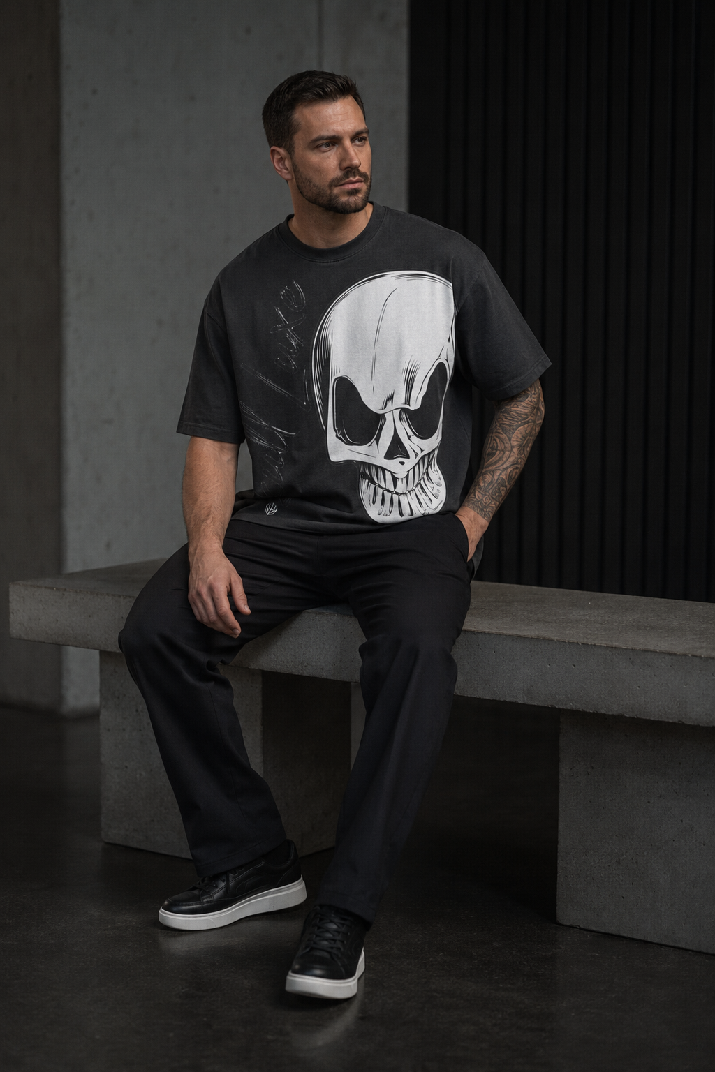 Model sitzt auf Betonbank und trägt schwarzes DREIZENTIA Skull Luxe Herren-T-Shirt mit großem weißem Totenkopf-Print
