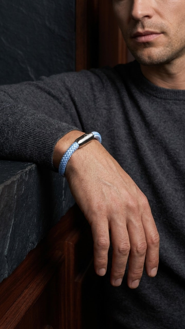 Hellblaues geflochtenes Armband mit silberfarbenem Dreizack Verschluss am Handgelenk eines Models mit grauem Pullover.