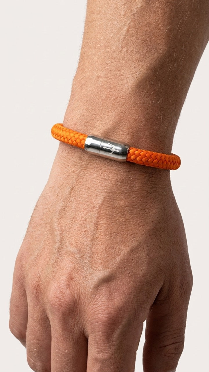 Orangefarbenes geflochtenes Armband mit silberfarbenem Dreizack Verschluss am Handgelenk in Studio-Seitenansicht.