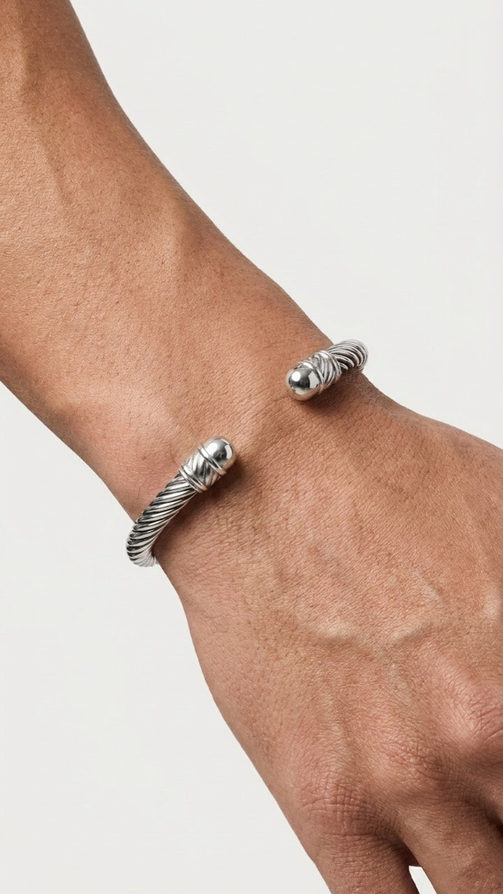 Silberfarbener Armreif mit gedrehtem Design am Handgelenk vor hellem Studiohintergrund.