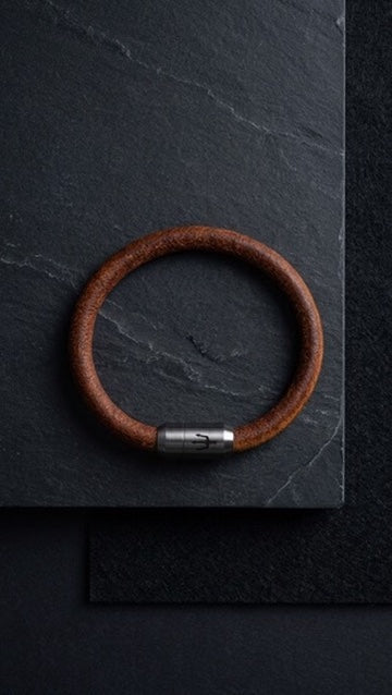 Braunes Lederarmband mit silberfarbenem Verschluss auf dunklem Schiefer