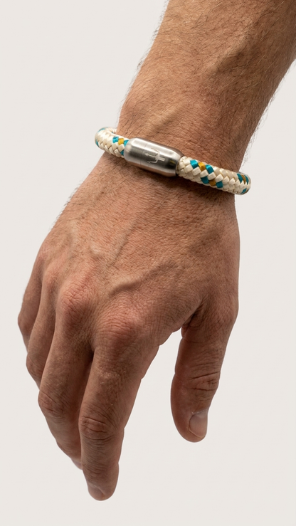 Beige braunes blaues geflochtenes Armband mit silberfarbenem Dreizack Verschluss am Handgelenk vor hellem Studiohintergrund.
