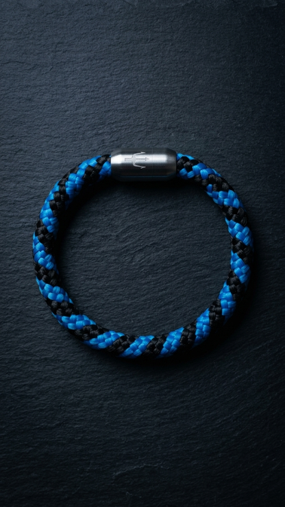 Blau schwarzes geflochtenes segeltauarmband mit Edelstahlverschluss als Produktfoto auf dunklem Schiefer