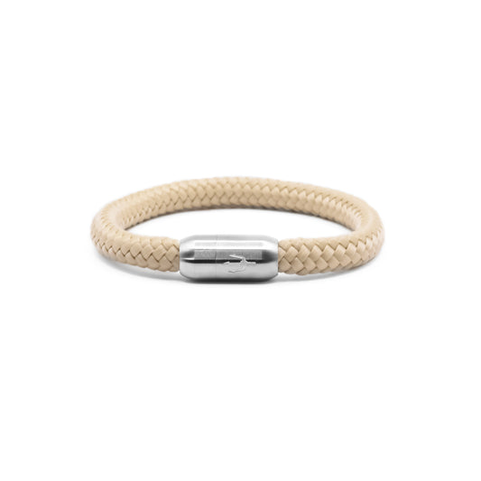 “Geflochtenes Armband in sanftem Beigeton mit einem Edelstahl-Magnetverschluss, verziert mit einem eingravierten Dreizack-Symbol. Elegantes und dezentes Design, inspiriert von natürlichen Sanddünen.”