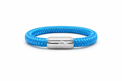 "Hellblaues Armband aus geflochtenem Segeltau mit einem Edelstahl-Magnetverschluss, verziert mit einem eingravierten Dreizack-Symbol. Frisches und modernes maritimes Design.”
