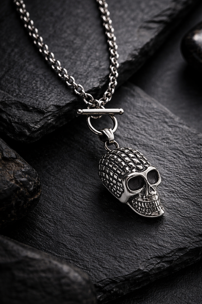 Silberfarbene Totenkopf-Halskette aus Edelstahl mit Gliederkette, als hochwertige Still-Life-Produktfotografie in dunkler, luxuriöser Premium-Ästhetik auf schwarzem Steinuntergrund.