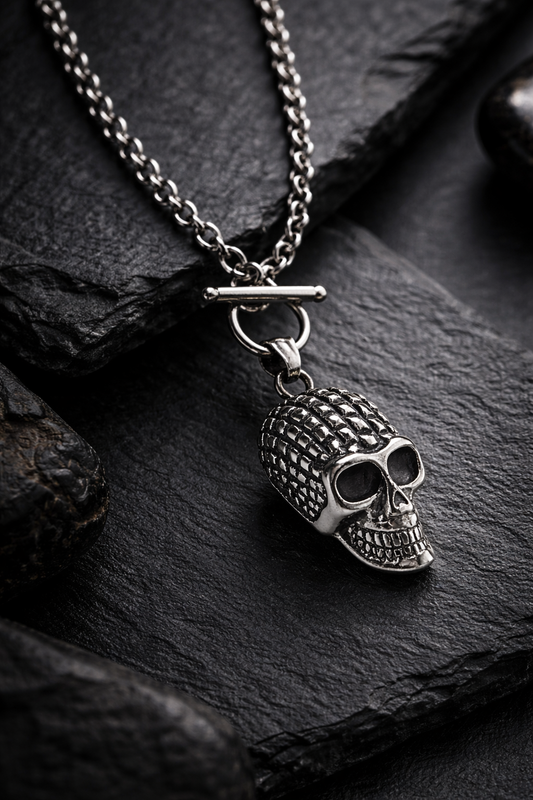 Silberfarbene Totenkopf-Halskette aus Edelstahl mit Gliederkette, als hochwertige Still-Life-Produktfotografie in dunkler, luxuriöser Premium-Ästhetik auf schwarzem Steinuntergrund.