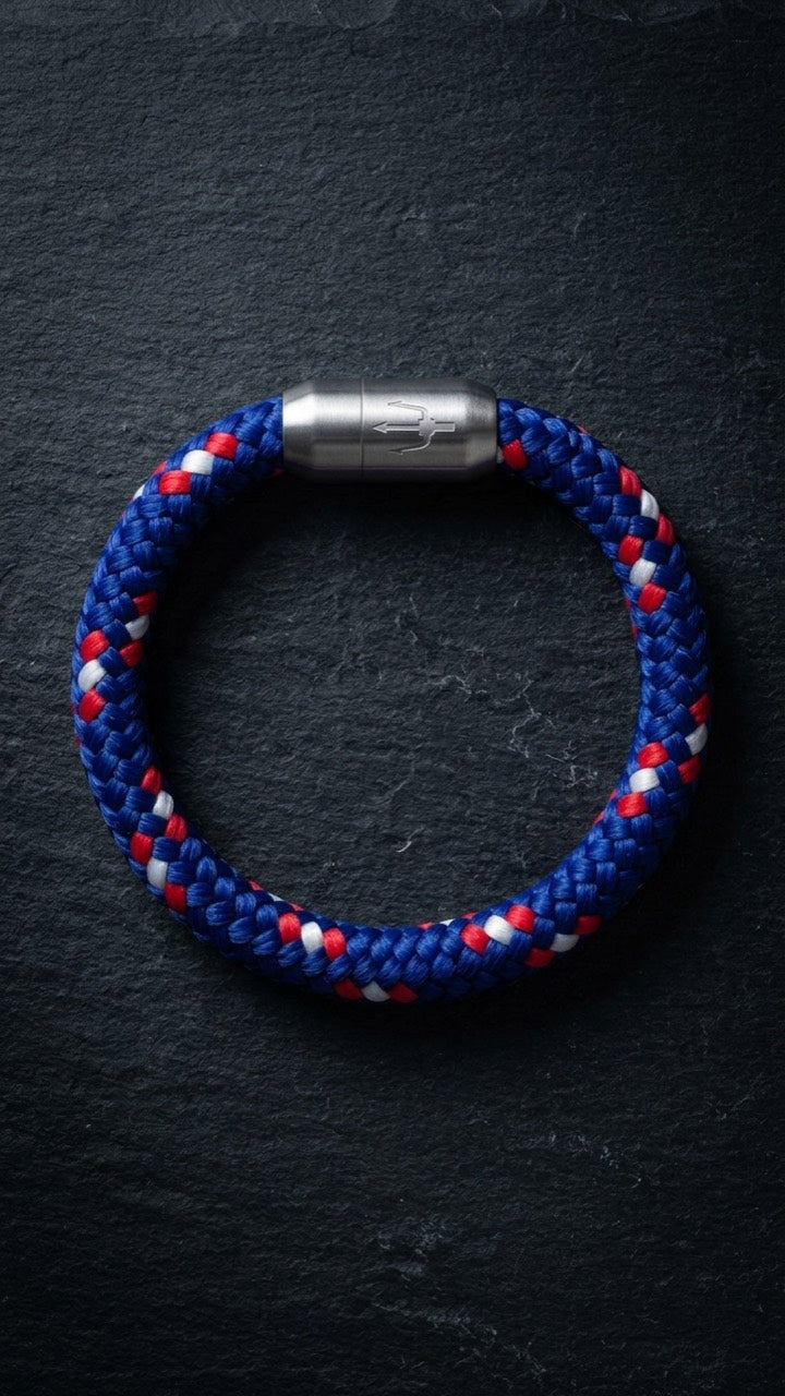 Blau-rot-weisses geflochtenes Armband mit silberfarbenem Dreizack Verschluss als Produktfoto auf dunklem Schiefer.