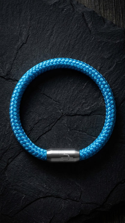Blaues geflochtenes Armband mit silberfarbenem Dreizack Verschluss als Produktfoto auf dunklem Schiefer.