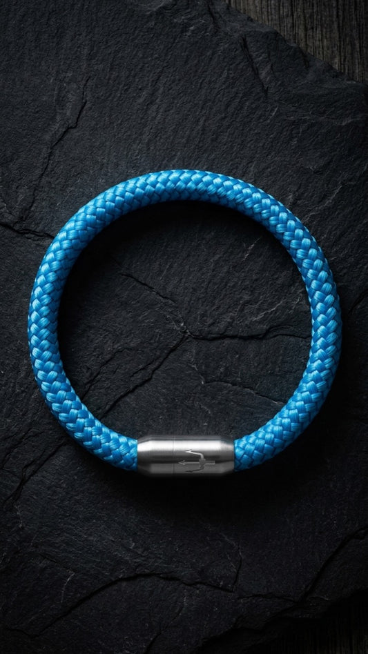 Blaues geflochtenes Armband mit silberfarbenem Dreizack Verschluss als Produktfoto auf dunklem Schiefer.
