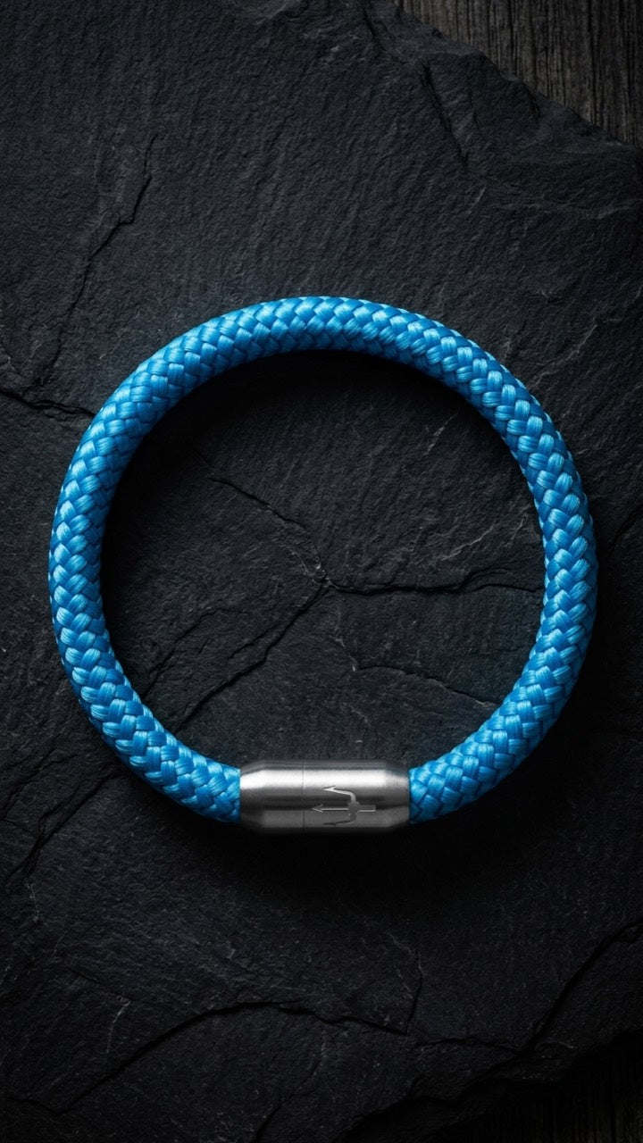 Blaues geflochtenes Armband mit silberfarbenem Dreizack Verschluss als Produktfoto auf dunklem Schiefer.