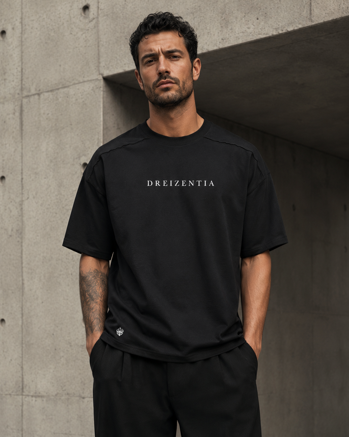 Model trägt schwarzes DREIZENTIA Essential Raw Herren-T-Shirt vor moderner Betonarchitektur