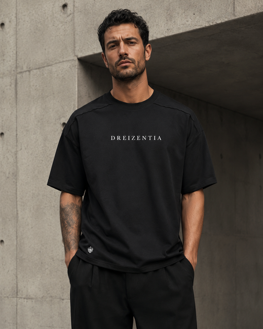 Model trägt schwarzes DREIZENTIA Essential Raw Herren-T-Shirt vor moderner Betonarchitektur