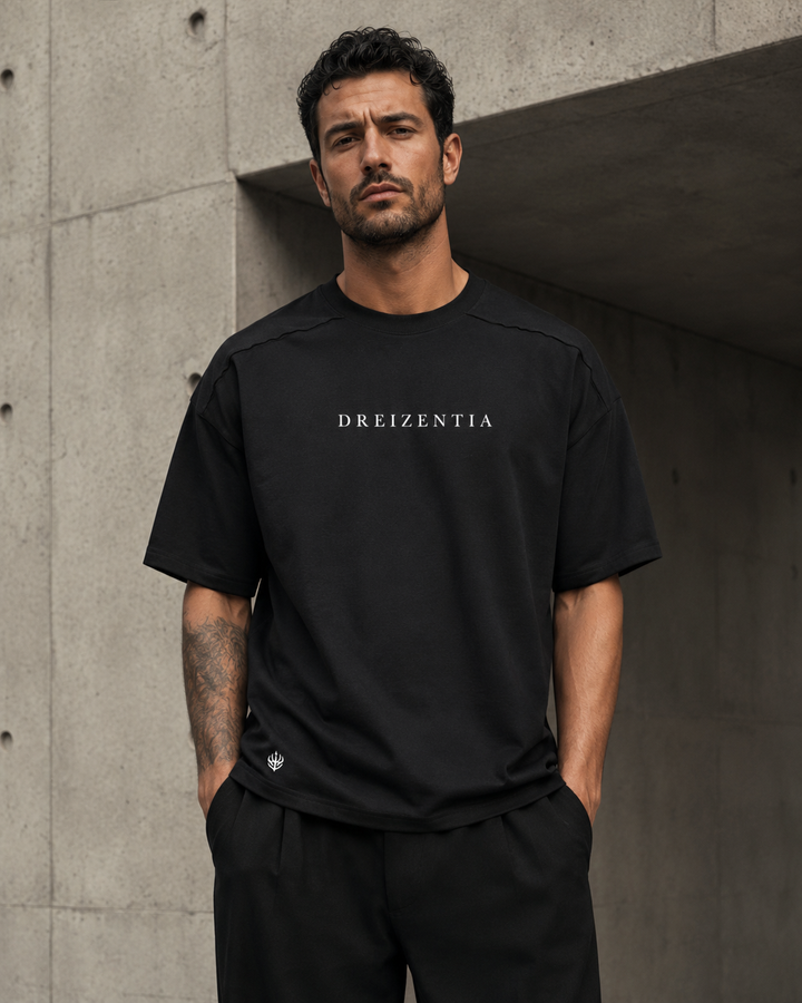 Model trägt schwarzes DREIZENTIA Essential Raw Herren-T-Shirt vor moderner Betonarchitektur