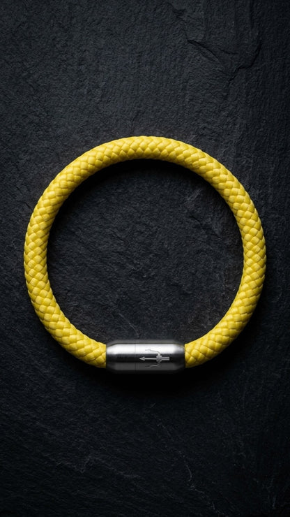 Gelbes geflochtenes Armband mit silberfarbenem Dreizack Verschluss als Produktfoto auf dunklem Schiefer.