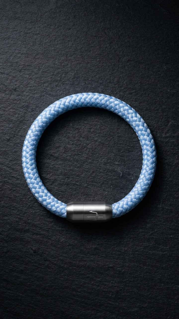 Hellblaues geflochtenes Armband mit silberfarbenem Dreizack Verschluss als zweite Produktansicht auf dunklem Schiefer.