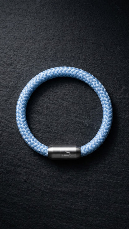 Hellblaues geflochtenes Armband mit silberfarbenem Dreizack Verschluss als zweite Produktansicht auf dunklem Schiefer.