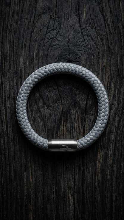 Hellgraues geflochtenes Seilarmband mit Edelstahlverschluss als Produktfoto auf dunklem Holz