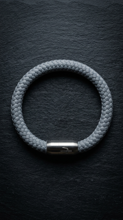 Hellgraues geflochtenes Seilarmband mit Edelstahlverschluss als Produktfoto auf dunklem Schiefer