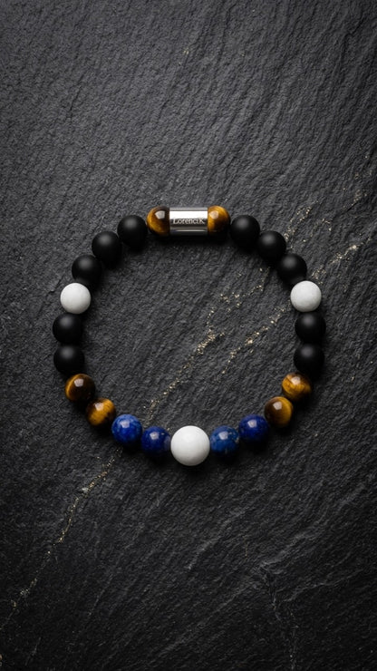 LorenciK Perlenarmband mit blauen Perlen, Tigerauge, weissen Perlen und schwarzen Akzenten auf dunklem Schiefer.