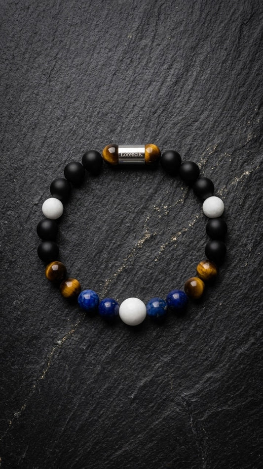 LorenciK Perlenarmband mit blauen Perlen, Tigerauge, weissen Perlen und schwarzen Akzenten auf dunklem Schiefer.