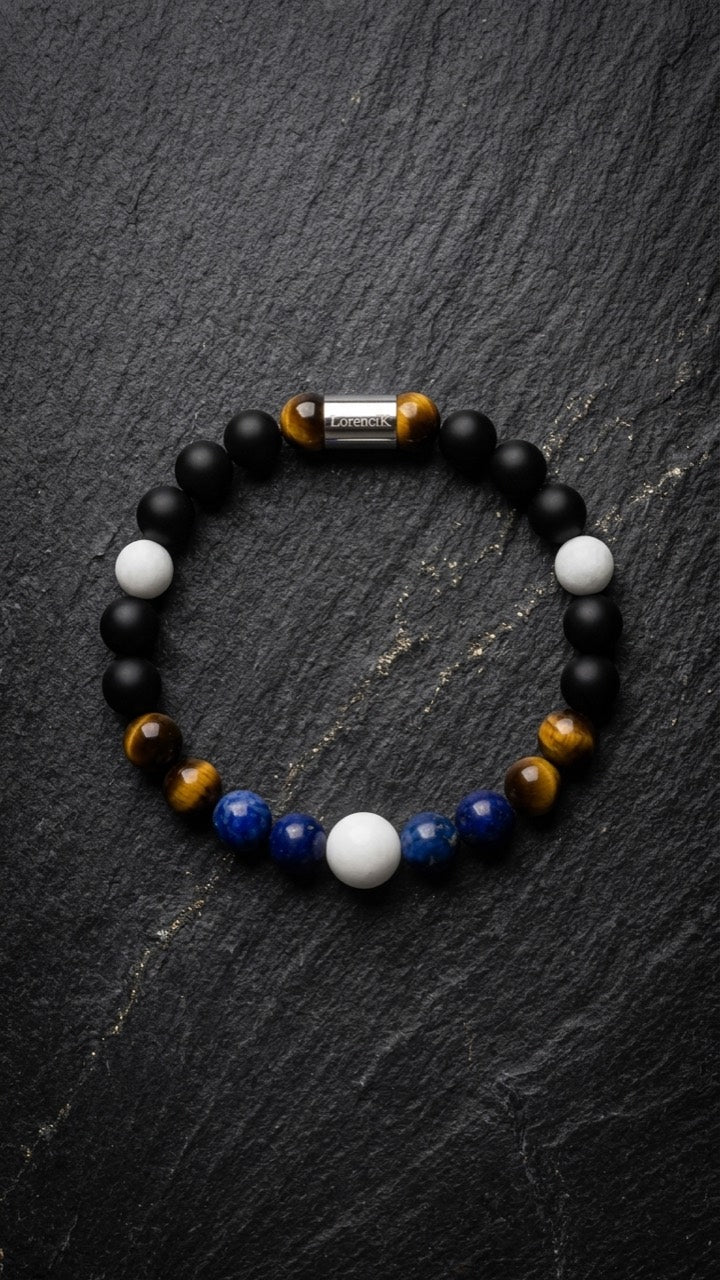 LorenciK Perlenarmband mit blauen Perlen, Tigerauge, weissen Perlen und schwarzen Akzenten auf dunklem Schiefer.