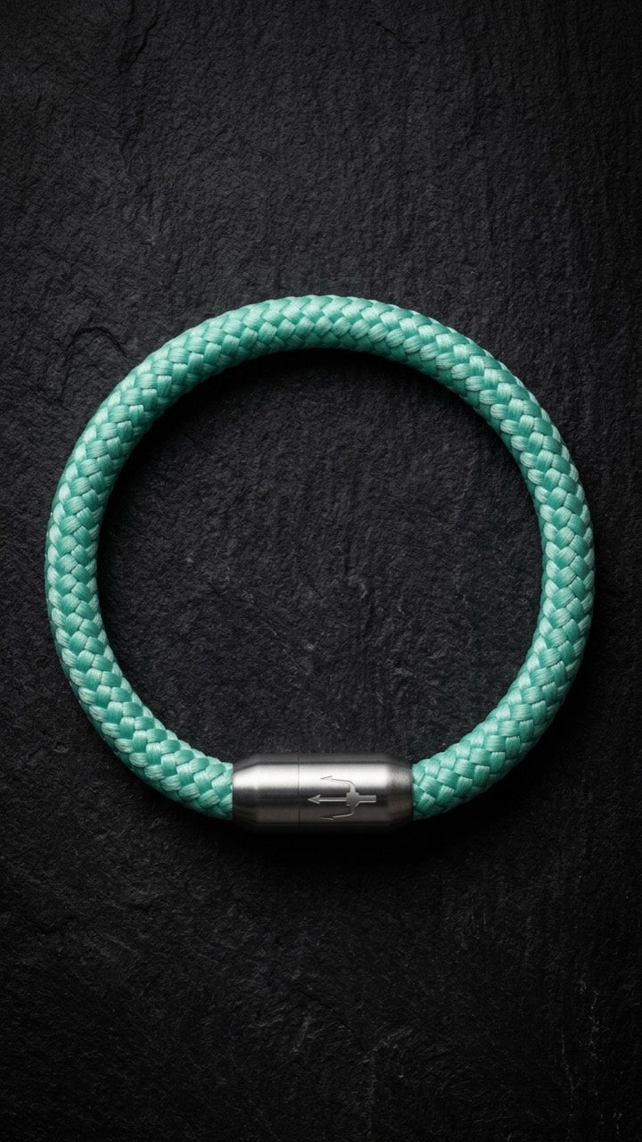 Mintfarbenes geflochtenes Armband mit silberfarbenem Dreizack Verschluss als Produktfoto auf dunklem Schiefer.