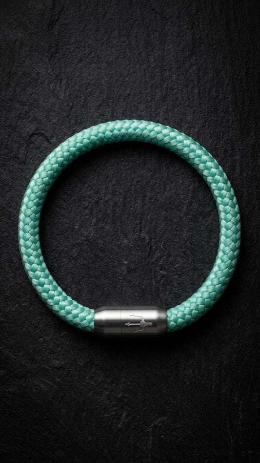 Mintfarbenes geflochtenes Armband mit silberfarbenem Dreizack Verschluss als Produktfoto auf dunklem Schiefer.