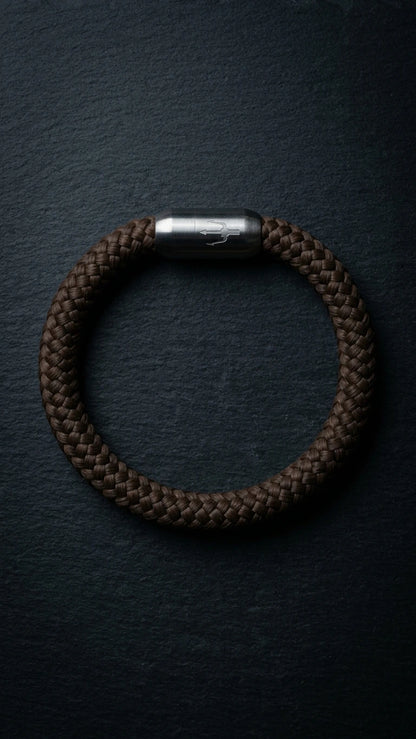 Nautic Force Dark Harbor – dunkelbraunes 8-mm-Segeltauarmband mit gebürstetem Edelstahlverschluss und Dreizack auf dunklem Schiefer