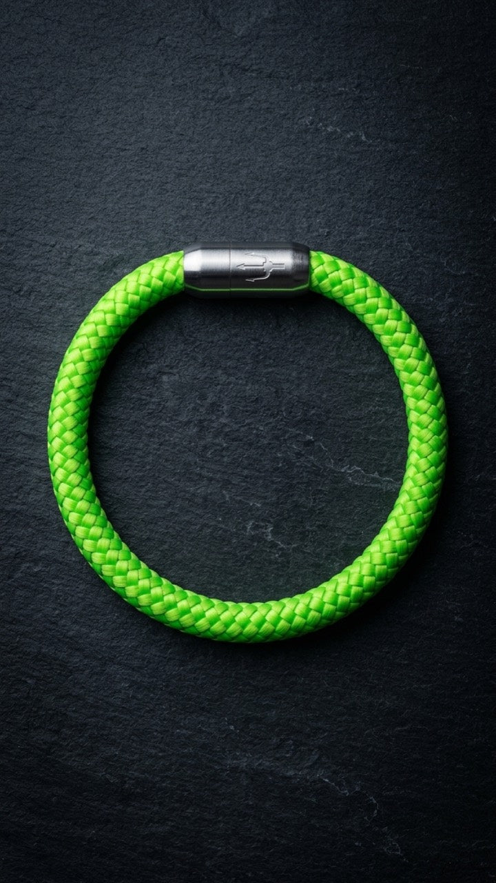Neongruenes geflochtenes Armband mit silberfarbenem Dreizack Verschluss als Produktfoto auf dunklem Schiefer.