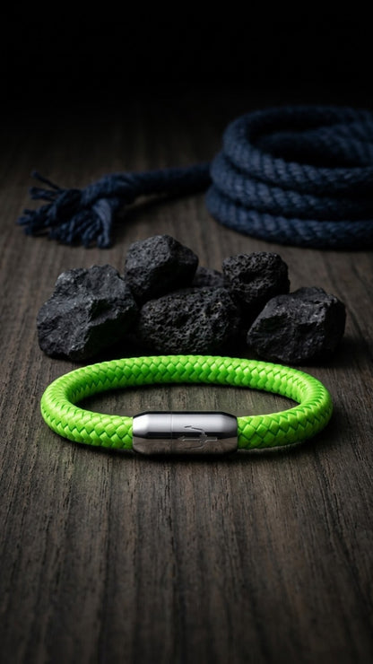 Neongruenes geflochtenes Armband mit silberfarbenem Dreizack Verschluss als Stillleben auf Holz mit Lavasteinen und Seil.