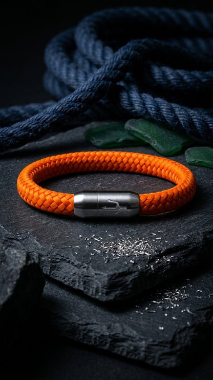 Orangefarbenes geflochtenes Armband mit silberfarbenem Dreizack Verschluss als Produktfoto auf dunklem Schiefer.