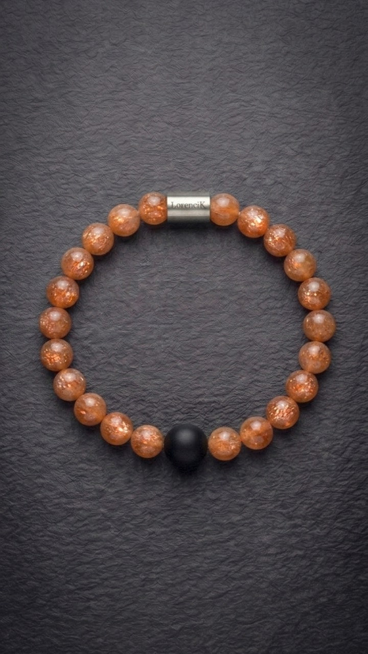 Orangefarbenes Perlenarmband mit Edelstahlverschluss und schwarzer Akzentperle auf dunklem Schiefer