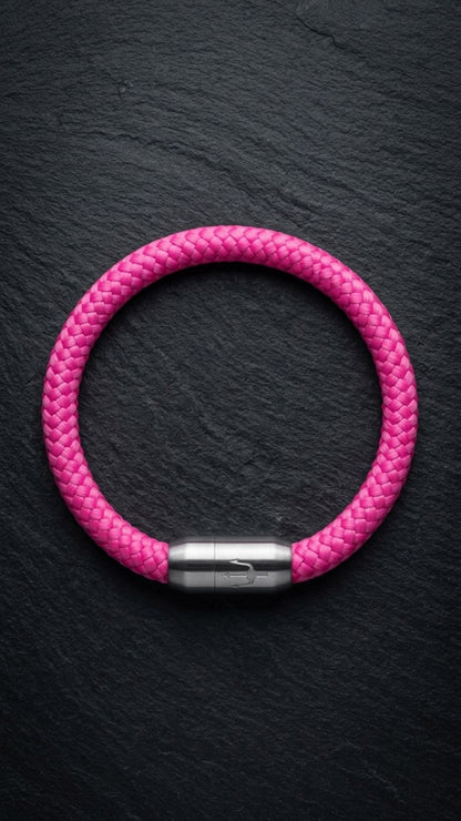 Pinkes geflochtenes Armband mit silberfarbenem Dreizack Verschluss als Produktfoto auf dunklem Schiefer.