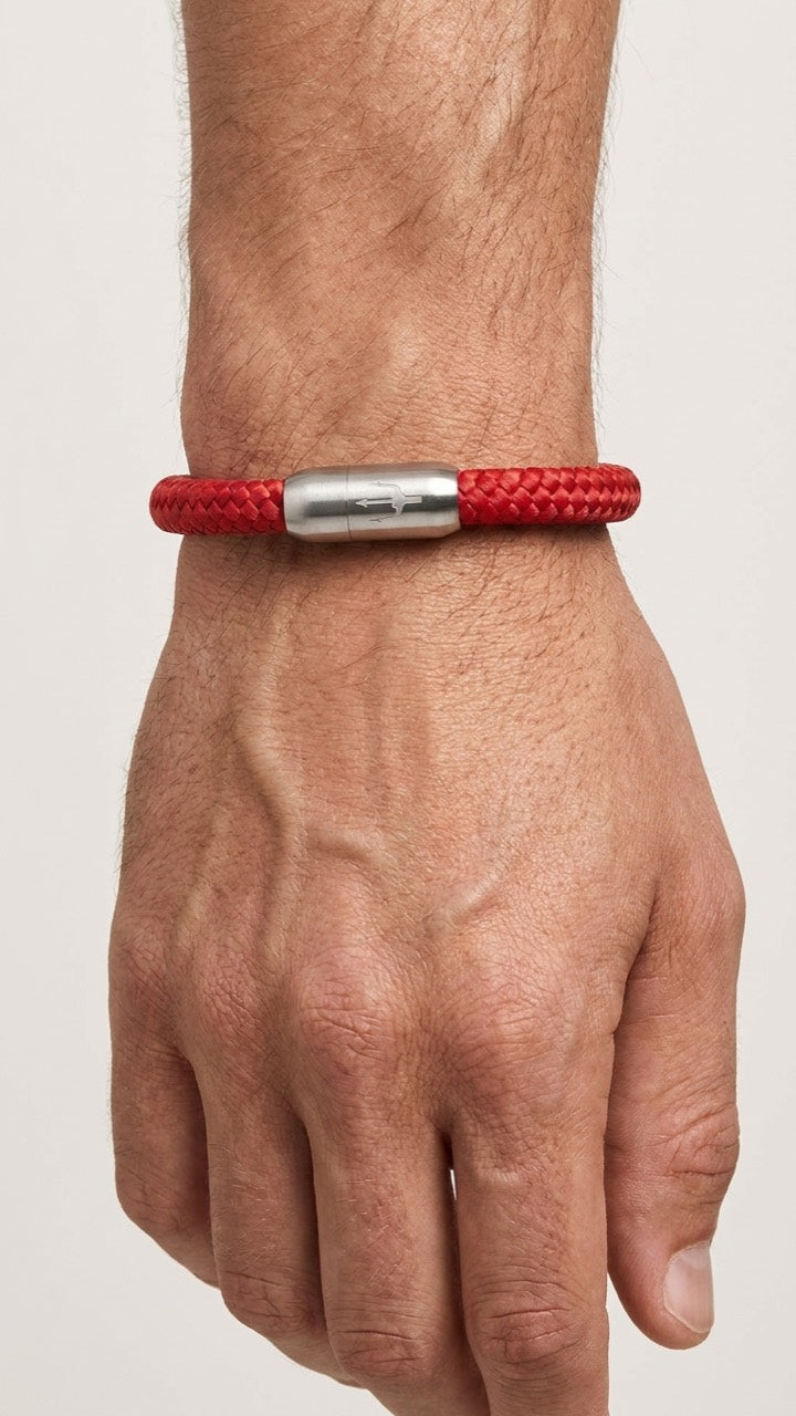 Rotes geflochtenes Armband mit silberfarbenem Dreizack Verschluss am Handgelenk vor hellem Studiohintergrund.