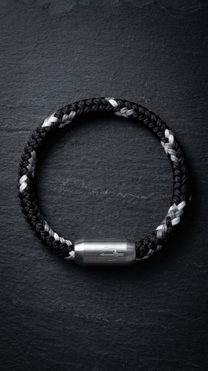 Schwarz-weisses geflochtenes Armband mit silberfarbenem Dreizack Verschluss als Produktfoto auf dunklem Schiefer.