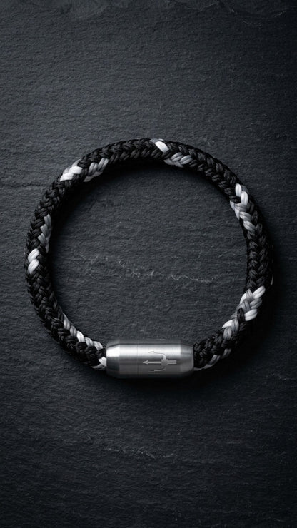 Schwarz-weisses geflochtenes Armband mit silberfarbenem Dreizack Verschluss als Produktfoto auf dunklem Schiefer.