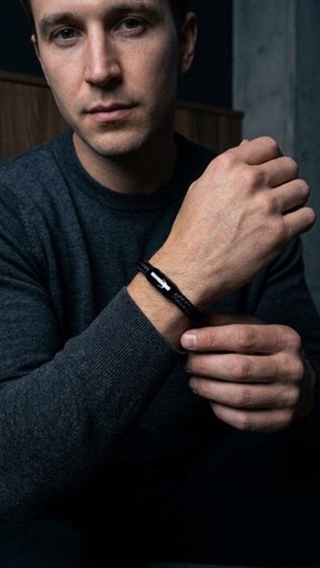 Schwarzes geflochtenes Herrenarmband am Handgelenk zu dunkelgrauem Pullover