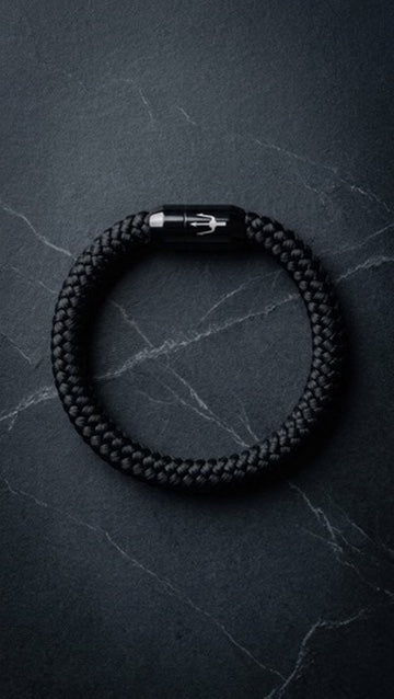 Schwarzes geflochtenes Herrenarmband mit dunklem Metallverschluss auf Schiefer