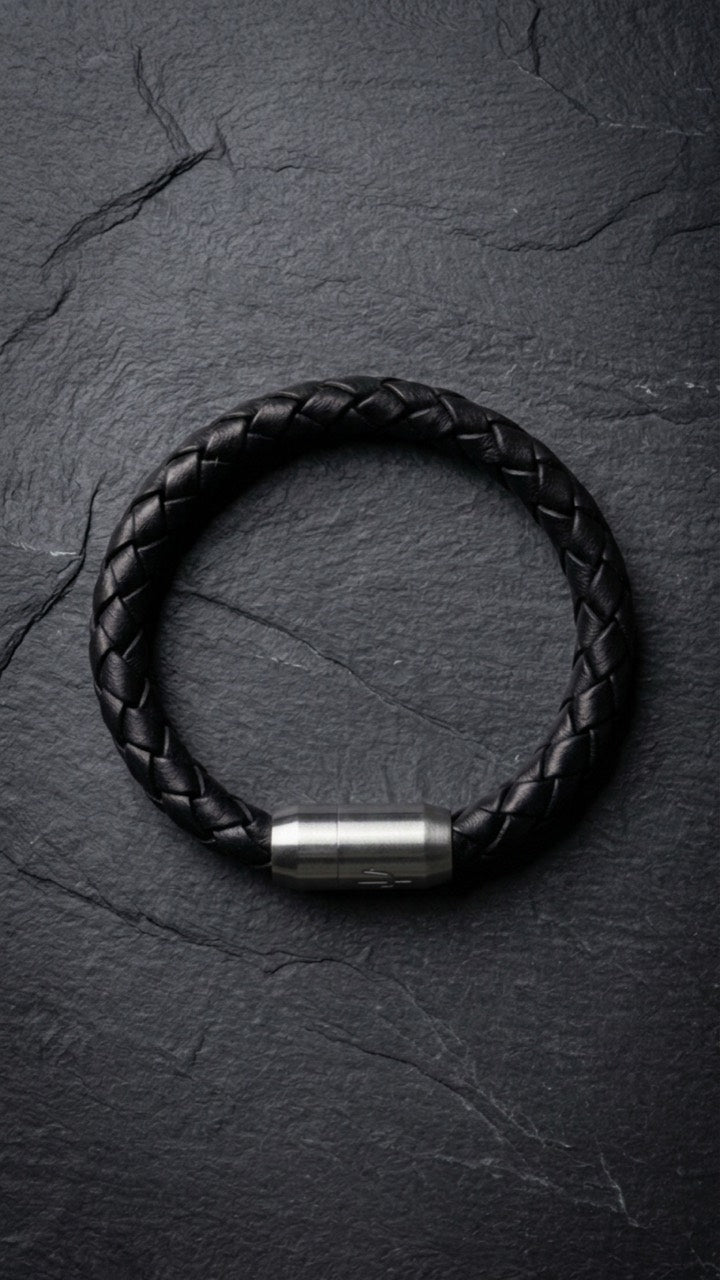 Schwarzes geflochtenes Lederarmband mit Edelstahlverschluss auf dunklem Schiefer