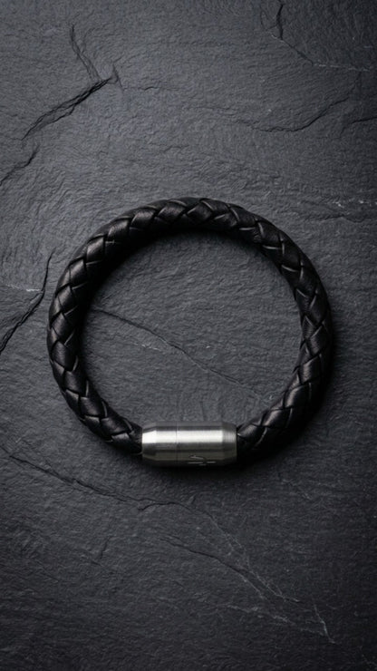 Schwarzes geflochtenes Lederarmband mit Edelstahlverschluss auf dunklem Schiefer