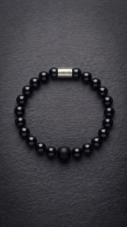 Schwarzes glänzendes Perlenarmband mit Edelstahlverschluss auf dunklem Schiefer