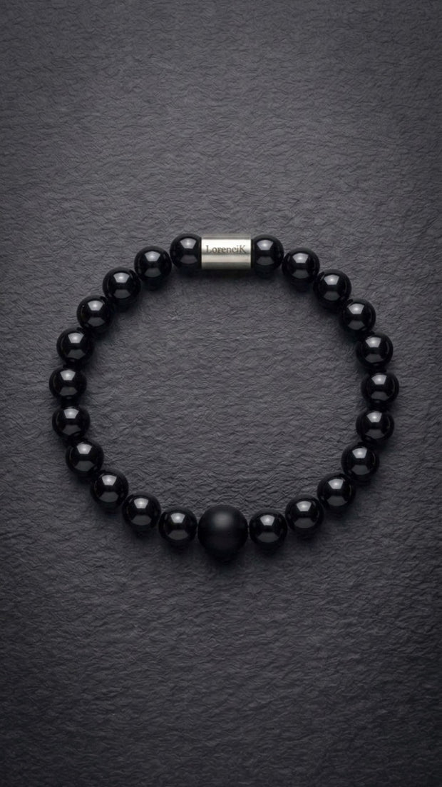 Schwarzes glänzendes Perlenarmband mit Edelstahlverschluss auf dunklem Schiefer