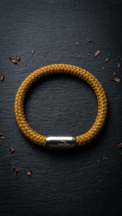 Senfgelbes geflochtenes Seilarmband mit Edelstahlverschluss als Produktfoto auf dunklem Schiefer