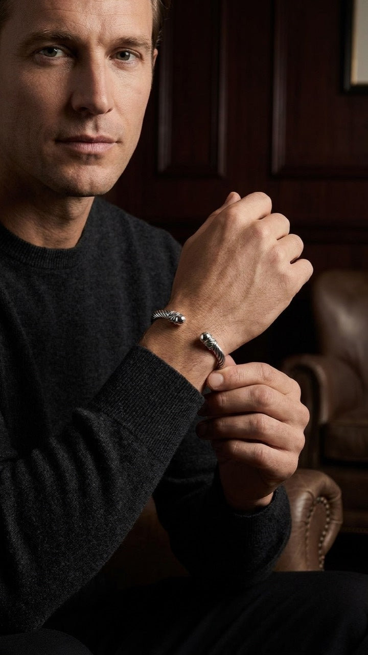 Silberfarbener Armreif im Federdesign am Handgelenk eines Models mit dunklem Pullover.