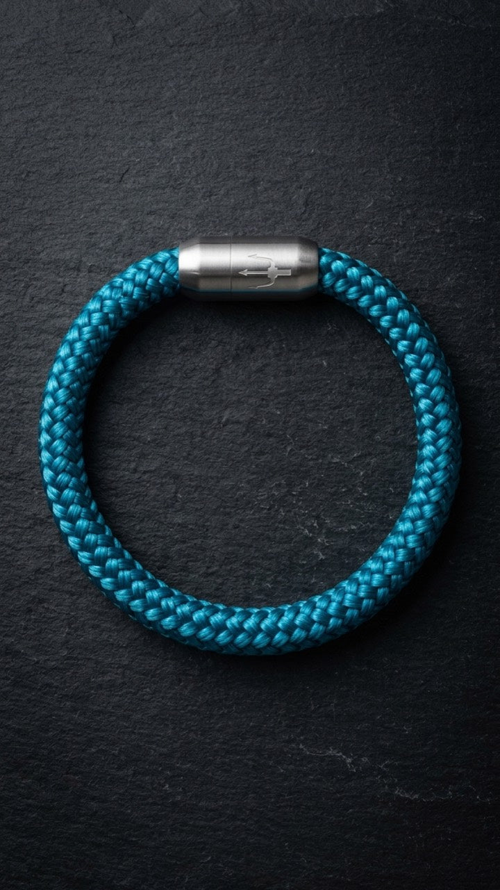 Tuerkisfarbenes geflochtenes Armband mit silberfarbenem Dreizack Verschluss als Produktfoto auf dunklem Schiefer.