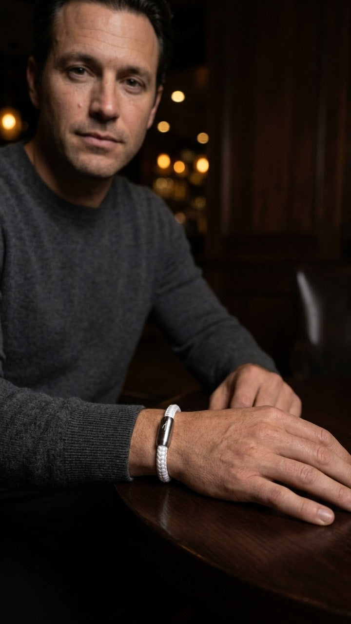 Weißes geflochtenes Seilarmband mit Edelstahlverschluss am Handgelenk eines Mannes am Tisch