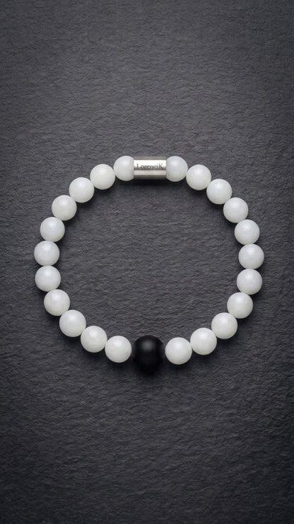 Weißes Perlenarmband mit Edelstahlverschluss und schwarzer Akzentperle auf dunklem Schiefer