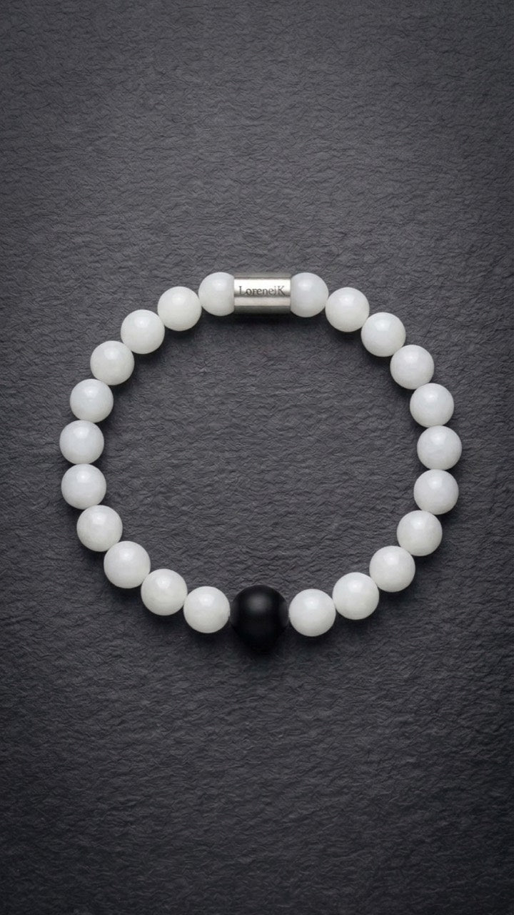 Weißes Perlenarmband mit Edelstahlverschluss und schwarzer Akzentperle auf dunklem Schiefer