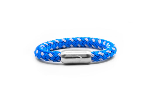 “Maritimes Armband aus geflochtenem Segeltau in kräftigen Blau- und Weißtönen, kombiniert mit einem Edelstahl-Magnetverschluss, verziert mit einem eingravierten Dreizack-Symbol. Ausdrucksstarkes und modernes Design für einen frischen Look.”